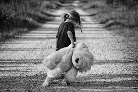 Little Girl holding a teddy bear walking down a dirt road